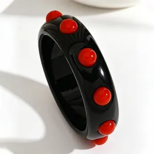 Detail view of a vintage-style black acrylic wide bangle with red polka dot inlays.