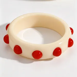 Close-up of a vintage cream acrylic wide bangle with raised red decorative polka dots