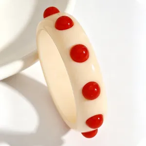 Detailed view of a retro cream-colored acrylic wide bangle featuring bold red dot studs