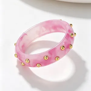 Detail of a pink marbled acrylic bangle bracelet featuring gold-tone stud embellishments