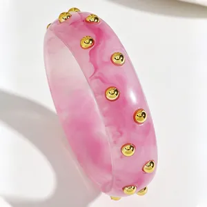 Macro view of a stylish retro pink marbled acrylic wide bangle featuring golden studs.