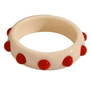 Close-up detail of a retro cream acrylic bangle with vibrant red polka dot studs.