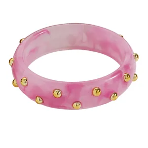 Macro view of a retro pink marbled acrylic bangle with elegant gold dot studs jewelry