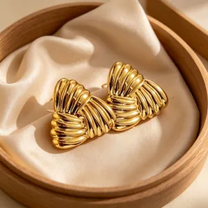 Dettaglio di orecchini d'oro strutturati su sfondo di raso beige in scatola di legno