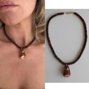 Dettaglio di una collana di perle marroni con ciondolo a conchiglia naturale stile spiaggia.