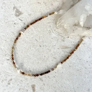 Dettaglio di una collana da spiaggia con conchiglie bianche e perline nei toni della terra.