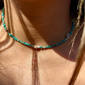Dettaglio di collana di perle turchesi con piccole conchiglie su pelle bagnata