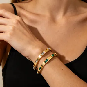 Close-up detail of gold-plated stainless steel bangles with white and green stones.