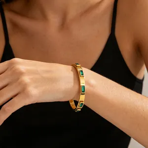 Elegant gold stainless steel bangle with emerald green baguette stones on wrist