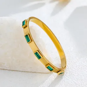 Close-up of gold stainless steel bangle featuring elegant rectangular green gemstones