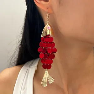 Gros plan d'une boucle d'oreille poisson à paillettes rouges et détails dorés.