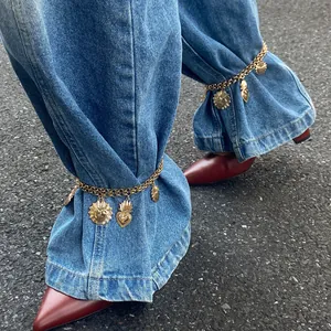 Trendy gold heart charm anklets used as decorative metal chain links on denim jeans.