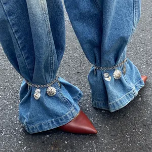 Detailed view of silver heart and sun charm anklets worn over denim jeans hems.