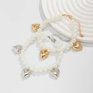 Close-up of pearl anklet set with gold and silver heart charms on white textured base