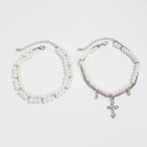 Detail view of layered pearl and silver chain anklet with vintage cross pendant