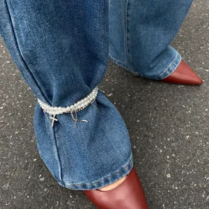 Close-up detail of double-layer faux pearl anklet with sparkling cross charms over denim jeans