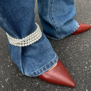 Trendy multi-layer faux pearl anklet worn over denim jeans as a unique fashion accessory