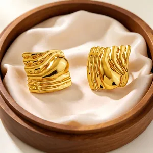 Close-up detail of gold-plated wavy square stainless steel earrings in a wooden tray.