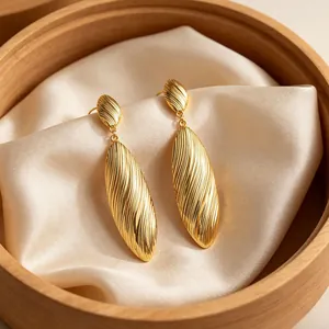 Elegant textured gold oval dangle earrings with a ribbed pattern on cream silk cloth