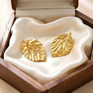 Detail of golden leaf-shaped stainless steel earrings on white silk in a wooden box