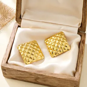 Close-up view of gold quilted square stud earrings displayed in a vintage wooden jewelry box.