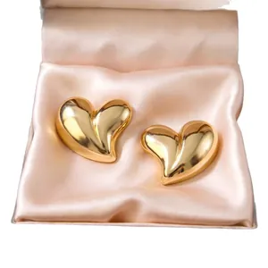 Elegant golden heart-shaped stainless steel stud earrings presented on pink satin padding