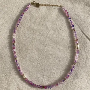Macro detail of a handmade necklace featuring purple natural stones and delicate pearls.