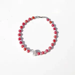 Detail view of handmade necklace with red natural stones and a single white pearl.