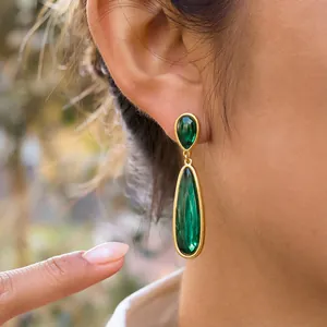 Dettaglio dei pendenti in acciaio dorato con eleganti pietre a goccia verde smeraldo.