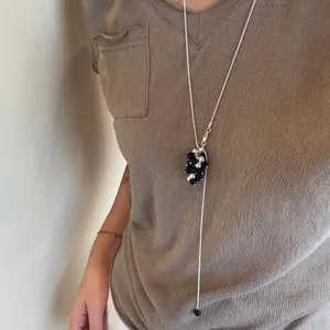 Detailed close-up of a long tassel sweater necklace with black and silver beads on a model