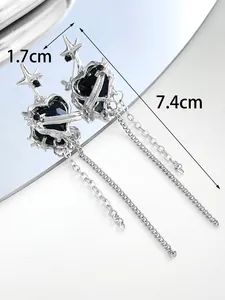 Close-up of silver tassel earrings with black heart stones and star details, showing size