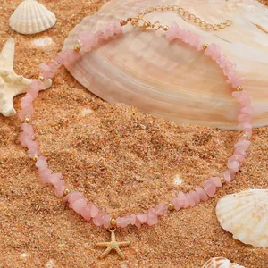 Primo piano di collana in pietra rosa con ciondolo a stella marina sulla sabbia.