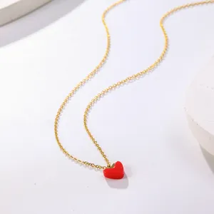 Close-up of a delicate gold chain necklace with a vibrant red heart oil-drop pendant.