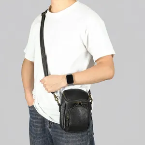 Petit sac bandoulière vertical en cuir noir pour homme, porté pour un style décontracté.