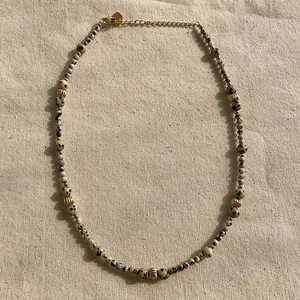 Close-up of dalmatian jasper beaded necklace with gold spacers on linen background