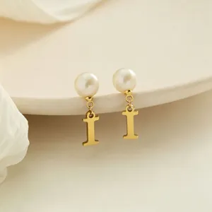 Dettaglio degli orecchini dorati con pendente lettera I e eleganti perle bianche.
