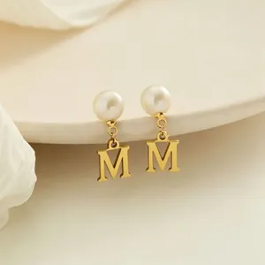 Dettaglio macro di eleganti orecchini in oro con ciondolo lettera M e perla bianca