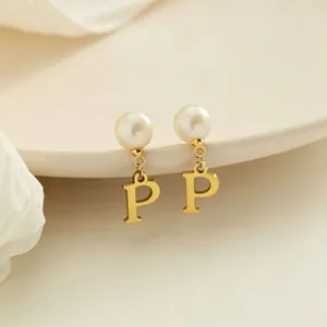 Dettaglio macro degli orecchini pendenti con lettera P in oro e perle bianche