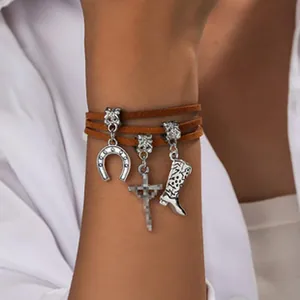 Gros plan sur un bracelet multi-rangs en daim marron style Western avec breloques cowboy.