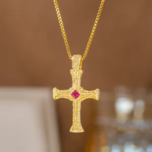 Detailansicht einer goldenen Kreuzkette mit strukturierter Oberfläche und rotem Stein