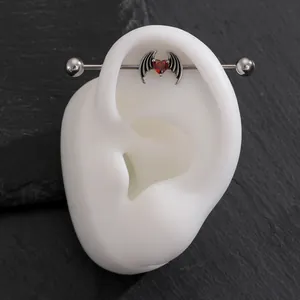 Gothic industrial barbell piercing with red heart and bat wings on dark stone background.