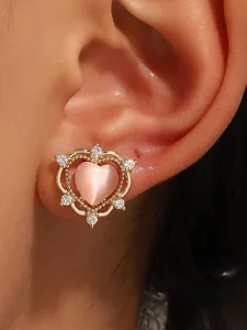 Detail of a gold heart-shaped clip-on earring with pink stone and small zircons on ear