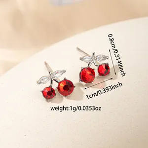 Elegant red crystal cherry stud earrings with white leaf detail on textured surface