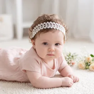 Macro detail of a white lace leaf headband worn by a cute baby lying on a soft white rug