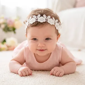 Adorable infant wearing a delicate white lace flower headband with sparkling rhinestones.