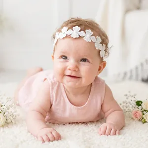 Detailed view of a delicate white lace flower headband with rhinestones worn by a baby