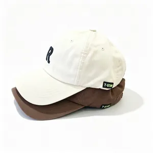 Vista detallada de dos gorras de béisbol apiladas en beige y marrón con bordado R