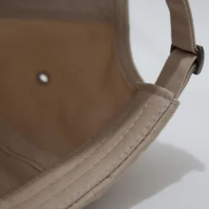 Primer plano de las costuras cuidadas y la hebilla ajustable en una gorra de algodón beige.