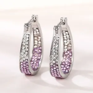 Close-up of silver-toned U-shaped hoop earrings with clear and purple crystal pavé