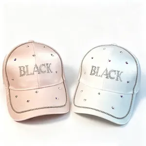 Détail de casquettes de baseball en satin rose et blanc avec lettrage BLACK en strass.